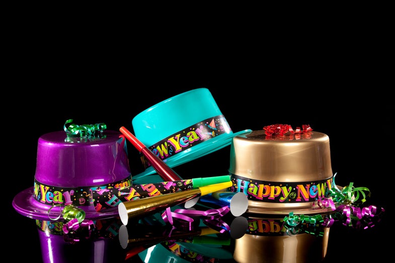 tři barevné plastové klobouky, které říkají šťastný nový rok na černém pozadí s hlukem a stuhami